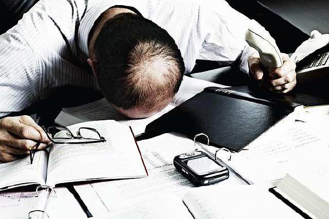 Totally desperate businessman with head on office desk top being overloaded with loads of work