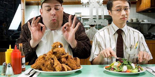 Man eating fried chicken as vegetarian looks on disapprovingly